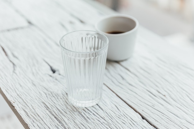 Verre clair et une tasse de café sur une table en bois peinte en blanc.