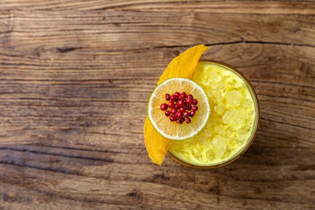 Un verre de cocktail d'ananas avec une garniture de grenade sur une table en bois.