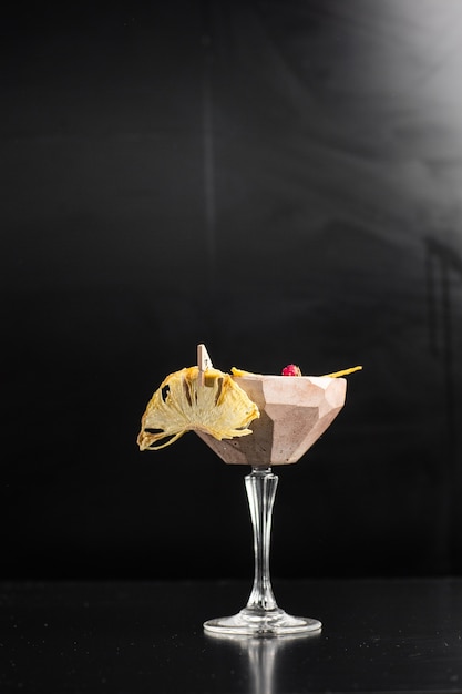 Verre à cocktail au citron jaune décoré d'ananas séché sur le bar sur fond noir