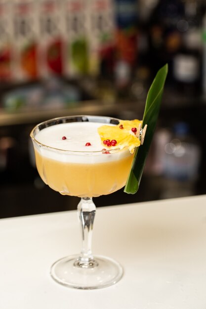 Verre avec cocktail au citron jaune décoré d'ananas séché et de menthe sur le bar flou