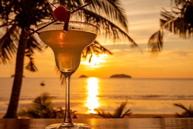 Verre à cocktail décoré d'une tranche de citron vert et de cerise sur fond de mer et coucher de soleil