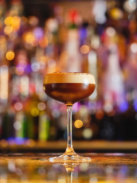 Un verre de cocktail d'espresso martini alcoolisé avec de la mousse blanche servi sur le comptoir d'un bar moderne sur un fond flou avec bokeh