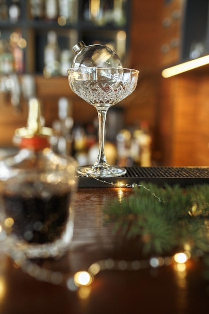 Verre à cocktail en forme de boule de Noël et babiole placé sur un comptoir en bois à ba