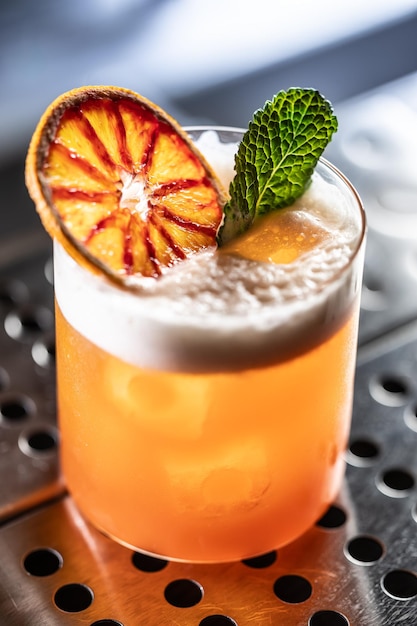 Un verre de cocktail Jungle Bird garni d'orange rouge séchée et de feuilles de menthe sur le comptoir du bar