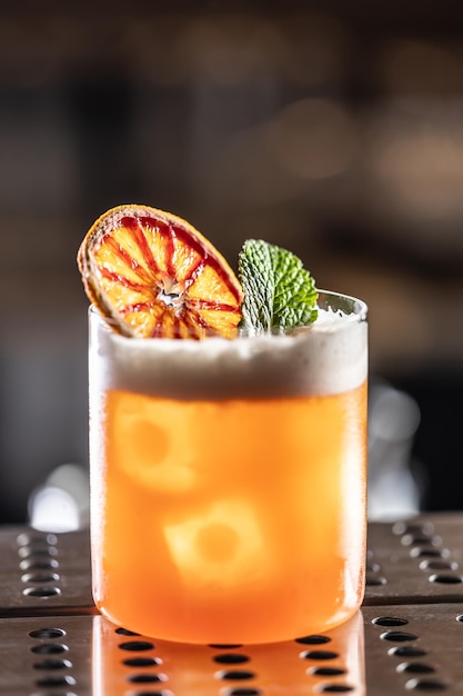 Un verre de cocktail Jungle Bird garni d'orange rouge séchée et de feuilles de menthe sur le comptoir du bar