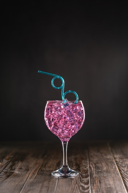 Un verre avec un cocktail rose rempli de glace sur une surface sombre