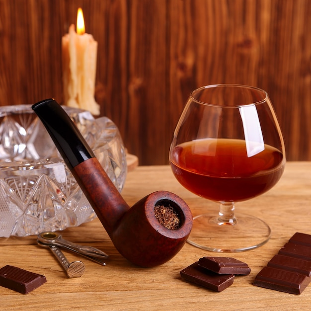 Un verre de cognac, de chocolat et de pipe sur la table en chêne