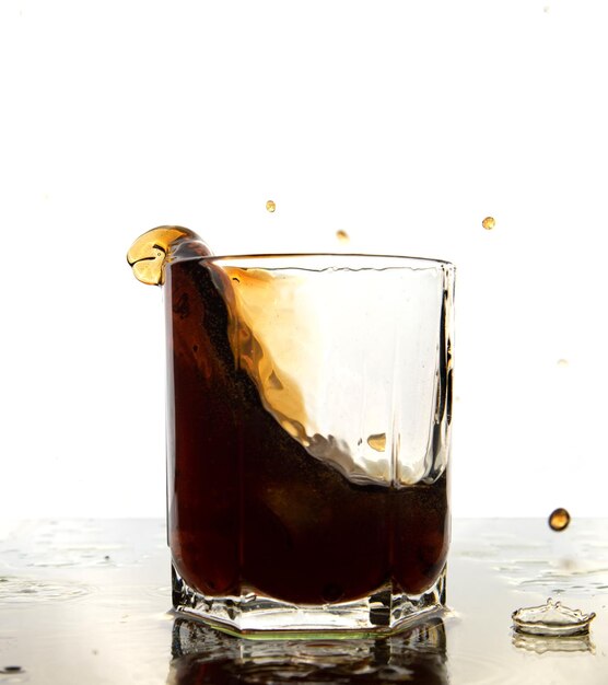 Verre de cola avec éclaboussures et glaçons sur blanc