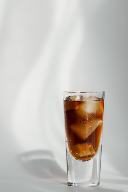 Verre de cola avec de la glace sur un mur blanc