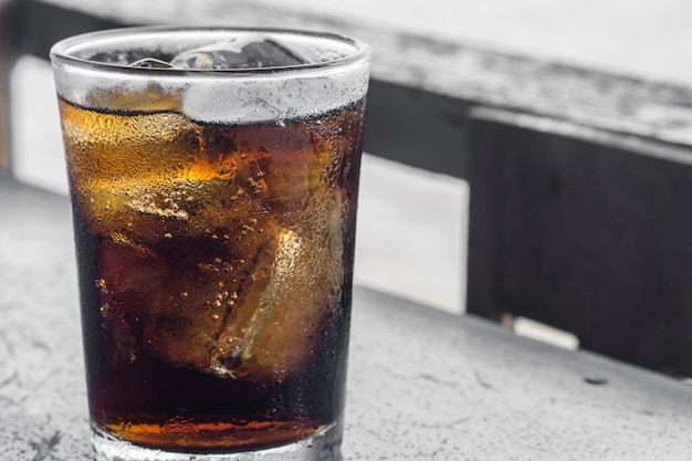 Verre de cola avec glace sur table en bois