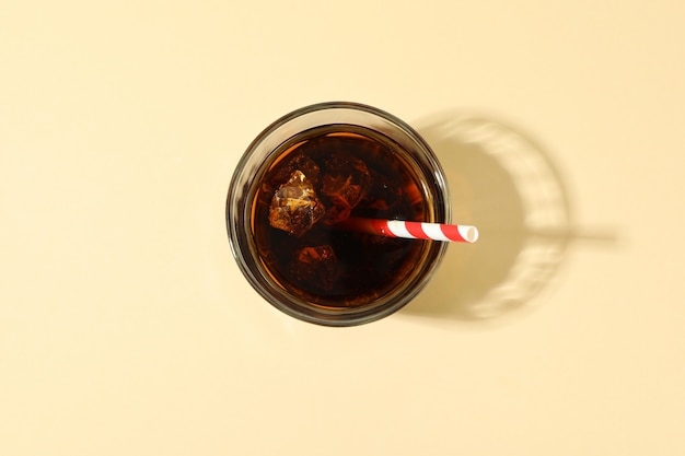 Verre de cola avec des glaçons et de la paille sur une surface beige