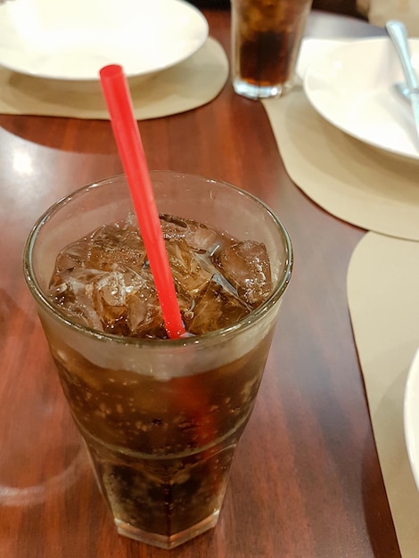 Un verre de cola en gros plan avec des cubes de glace et de la paille