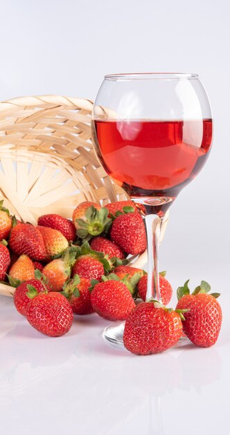 Verre en cristal avec du vin rose avec de belles fraises sur une surface blanche, mise au point sélective.