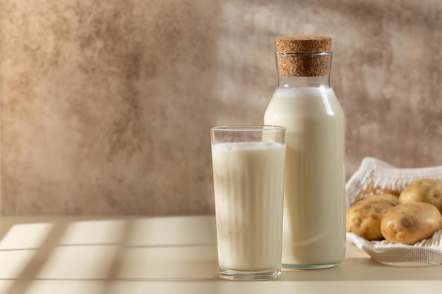 Un verre et une cruche de lait de pomme de terre avec des pommes de terre crues dans un bol Espace de copie