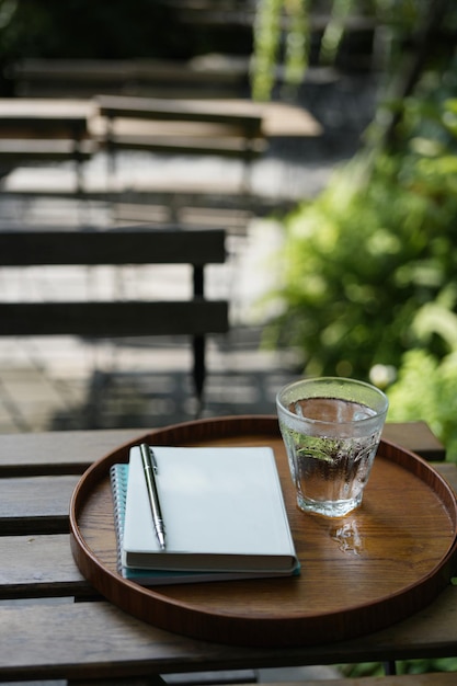 Un verre d'eau et un bloc-notes à l'intérieur d'un plateau en bois sur une table en bois