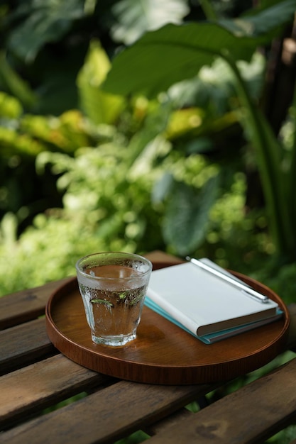 Un verre d'eau et un bloc-notes à l'intérieur d'un plateau en bois sur une table en bois