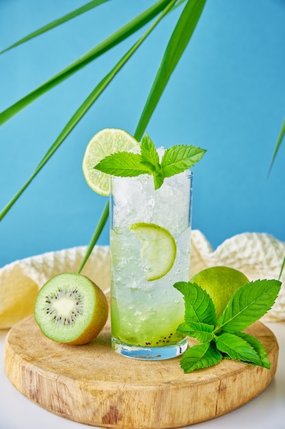 Verre d'eau avec citron vert kiwi et menthe sur fond bleu