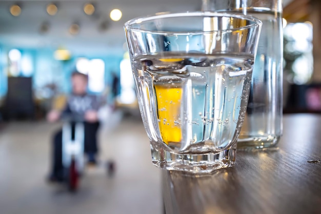 Le verre avec de l'eau claire se tient sur le bord d'une table en bois laissée négligemment