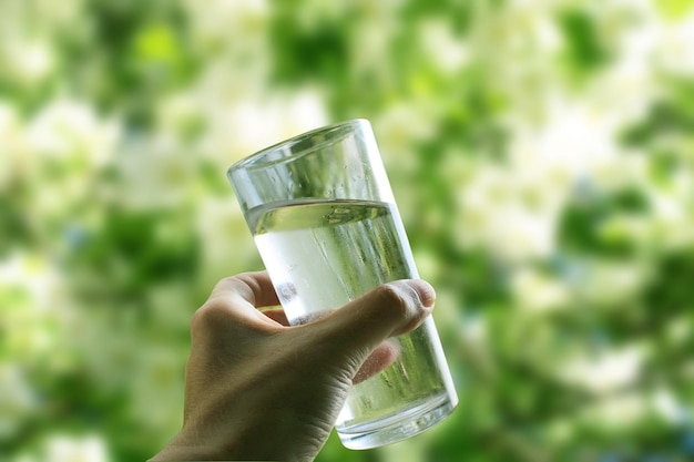 Un verre d'eau dans une main en gros plan sur un fond vert naturel à l'extérieur