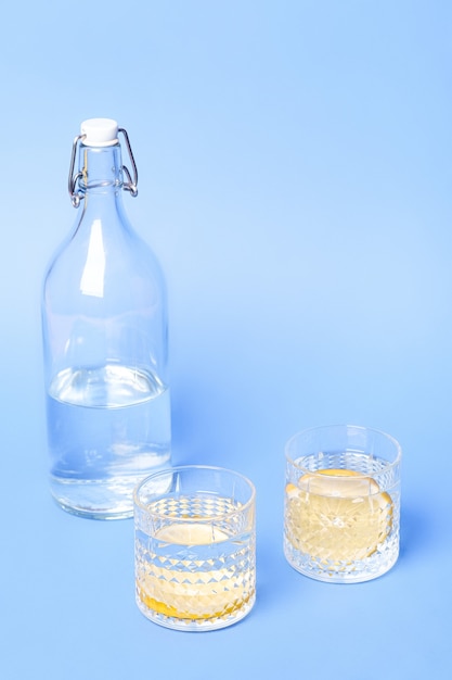 Verre avec de l'eau et du citron près de la bouteille sur une surface bleue