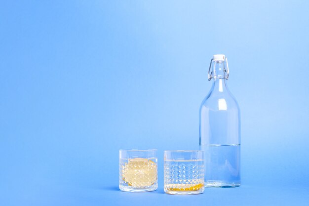 Verre avec de l'eau et du citron près de la bouteille sur une surface bleue