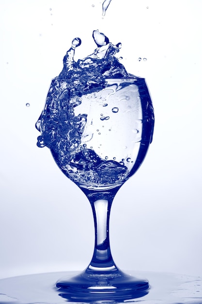 Photo verre d'eau. éclaboussure d'eau dans un verre à vin sur fond bleu