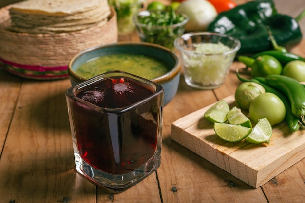 Verre avec de l'eau de fleur d'hibiscus fraîche au premier plan sur une table avec des tortillas sauce verte et légumes