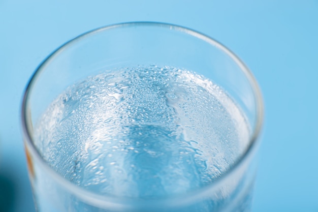 Verre d'eau froide pure sur un gros plan de fond bleu humide.