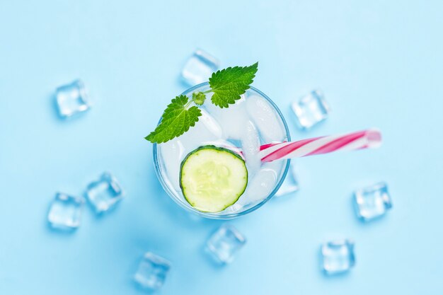 Verre d'eau froide et rafraîchissante avec de la glace, de la menthe et du concombre sur fond bleu. Glaçon. Concept d'été chaud, alcool, boisson rafraîchissante, étancher la soif, bar. Mise à plat, vue de dessus