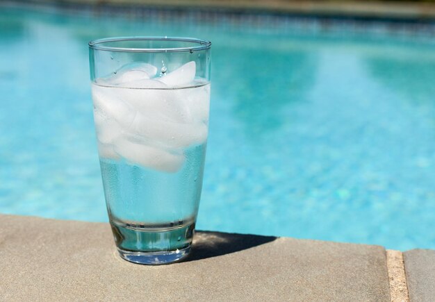 Verre d'eau avec des glaçons sur le côté de la piscine