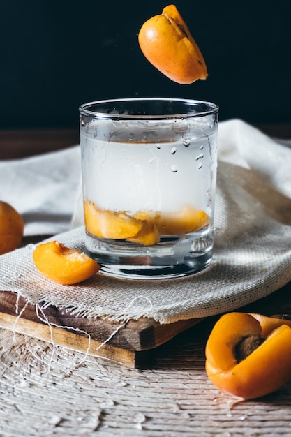 Verre d'eau avec des pêches sur nappe et planche de bois