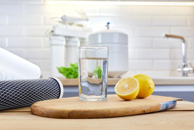 Verre d'eau propre avec des citrons et des cartouches de filtre à osmose inverse sur une table dans la cuisine