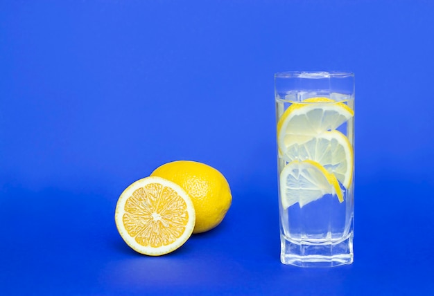 verre d'eau avec des quartiers de citron et du citron jaune sur fond bleu