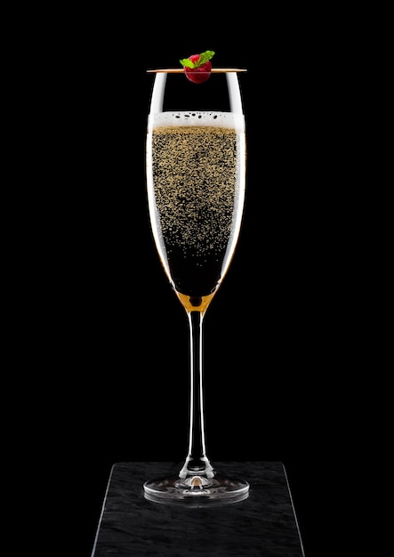 Verre élégant de champagne jaune avec framboise sur bâton sur panneau de marbre noir sur noir