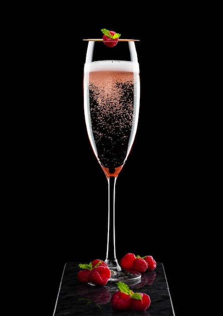 Verre élégant de champagne rose rose avec framboise sur bâton avec baies fraîches et feuille de menthe sur panneau de marbre noir sur noir