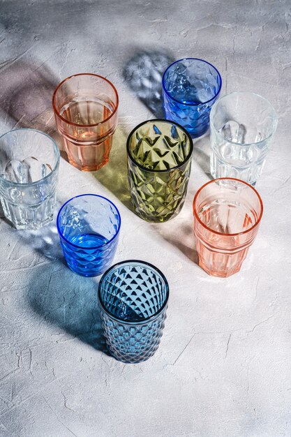 Verre à facettes et géométriques colorés, groupe de verres vides vert, rouge, bleu et transparent pour boisson sur surface de béton en pierre, vue d'angle