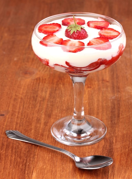 Verre de fraises mûres avec de la crème sur fond de bois