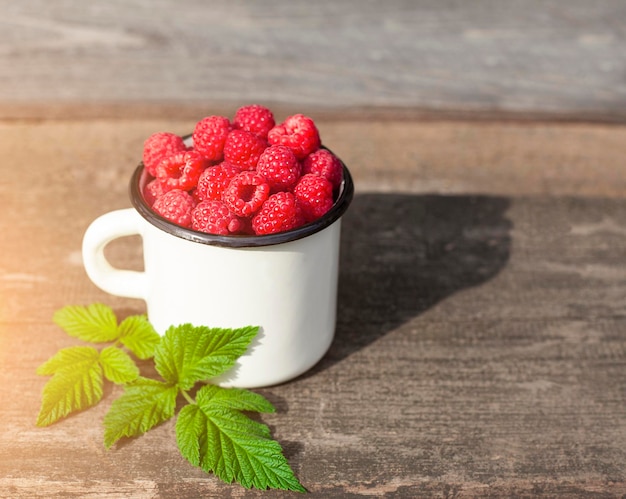 un verre de framboises au soleil sur une vieille surface en bois