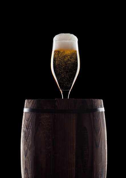 Verre froid de bière artisanale sur un vieux tonneau en bois sur fond noir avec de la rosée et des bulles