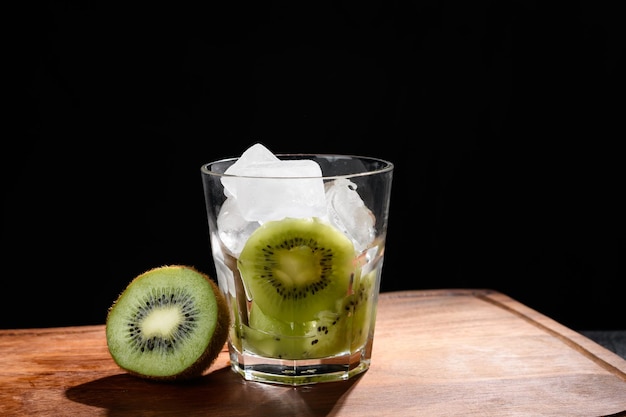 verre avec de la glace et des ingrédients de kiwi pour faire une boisson avec du kiwi sur fond noir