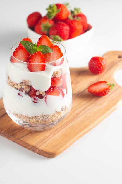 Verre avec granola, yaourt et fraises fraîches sur tableau blanc. Concept de bol de petit-déjeuner sain.