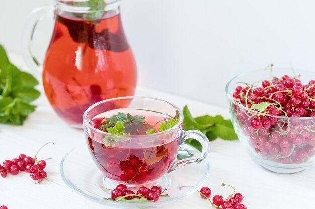 Verre de groseille dans une carafe en verre transparent et une tasse Vase en verre transparent avec des baies de groseille rouge sur le fond en bois blanc