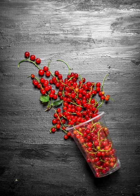 Verre de groseilles rouges sur table en bois noir.