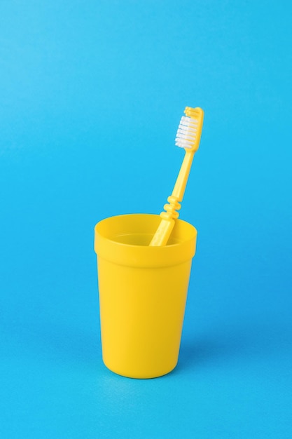 Un verre jaune avec une brosse à dents jaune sur fond bleu clair