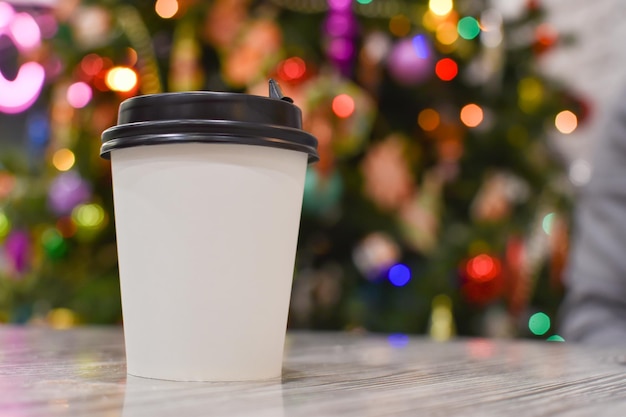 Un verre jetable en papier sur le fond d'un bokeh d'arbre de Noël coloré. Lumières brillantes lumineuses. Fond magique de Noël avec bokeh. Fête du nouvel an. Flatlay, vue de dessus.