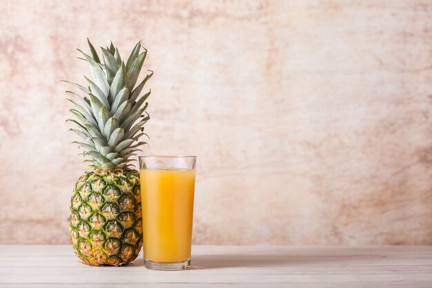 Verre de jus d'ananas frais avec des fruits crus sur bois