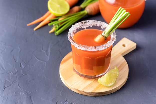 Verre de jus de carotte et carottes fraîches sur plateau en bois fond gris Copy Space