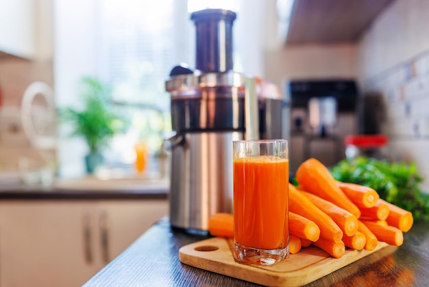 Un verre de jus de carotte fraîchement pressé et une centrifugeuse dans la cuisine
