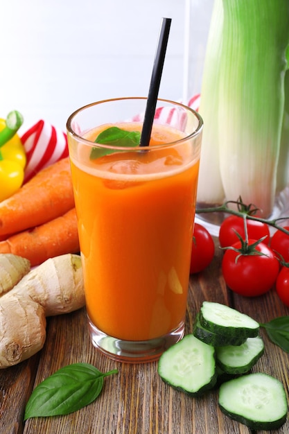 Verre de jus de carotte frais et légumes sur table en bois