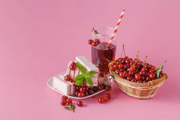 Verre de jus de cerise avec des baies de cerises fraîches sur fond rose.